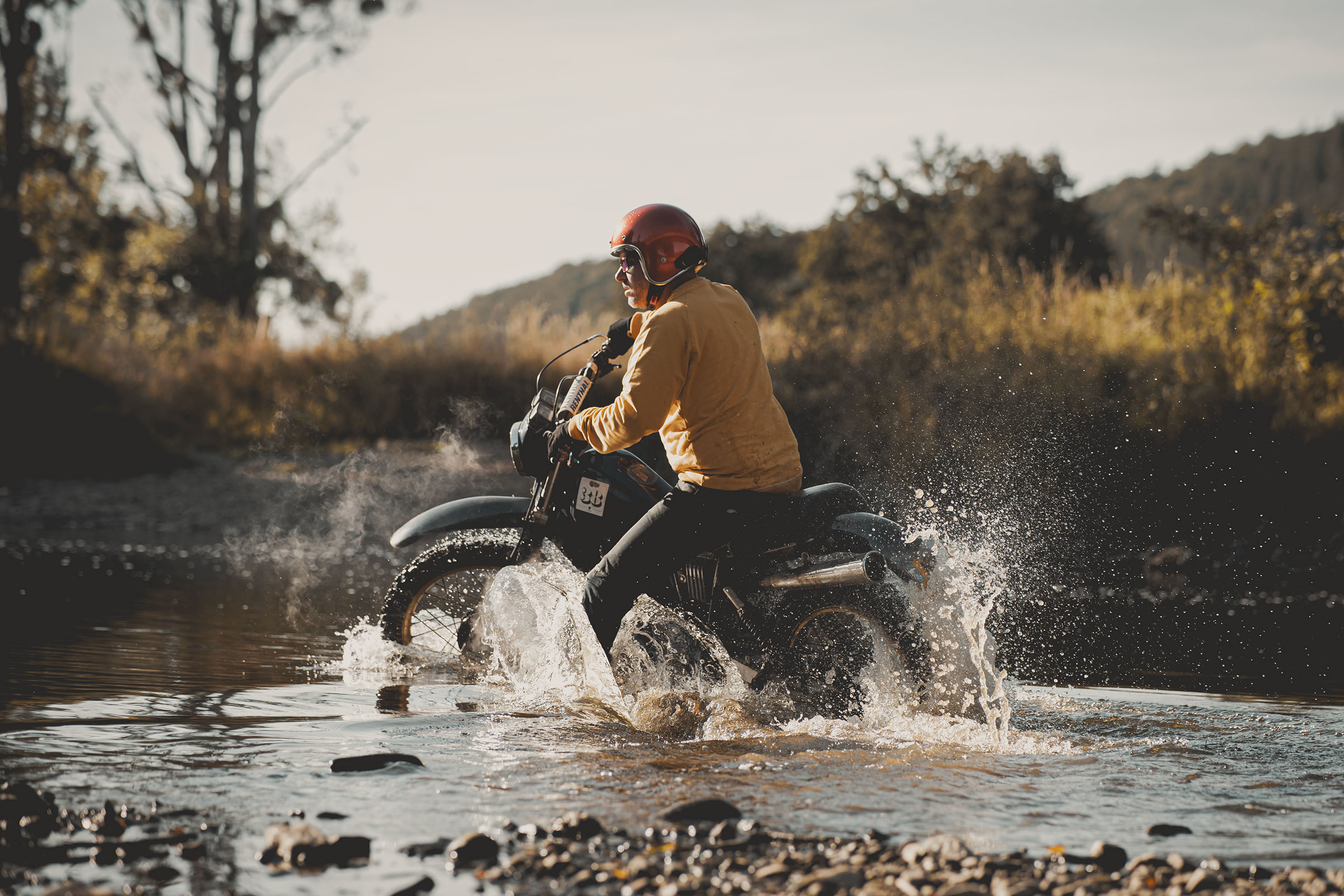 Merk belevenis via een etoere outdoor brandingfoto van een motorrijder die door een ondiepe rivier rijdt tijdens een offroad avontuur